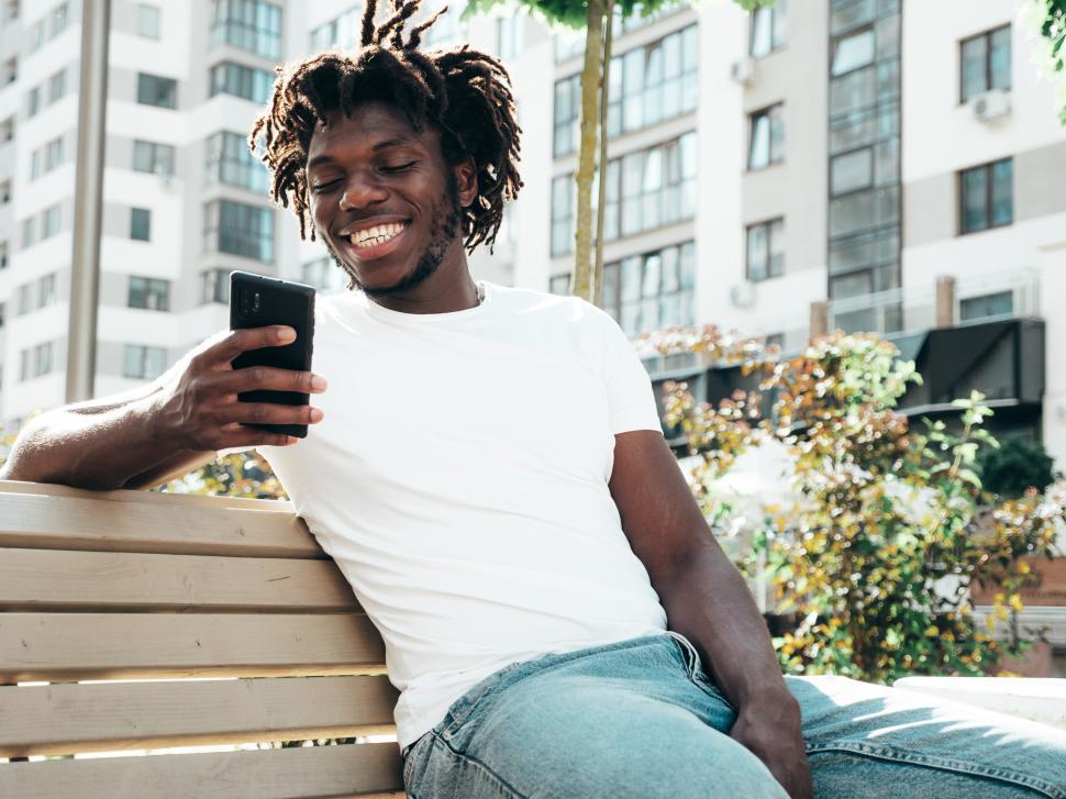 Free Image of Man smiling at phone while sitting on park bench outdoors 