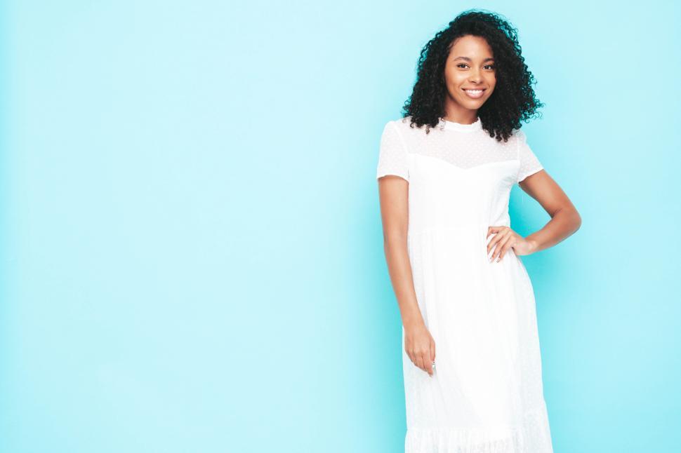 Free Image of Cheerful woman in elegant white dress against blue backdrop 