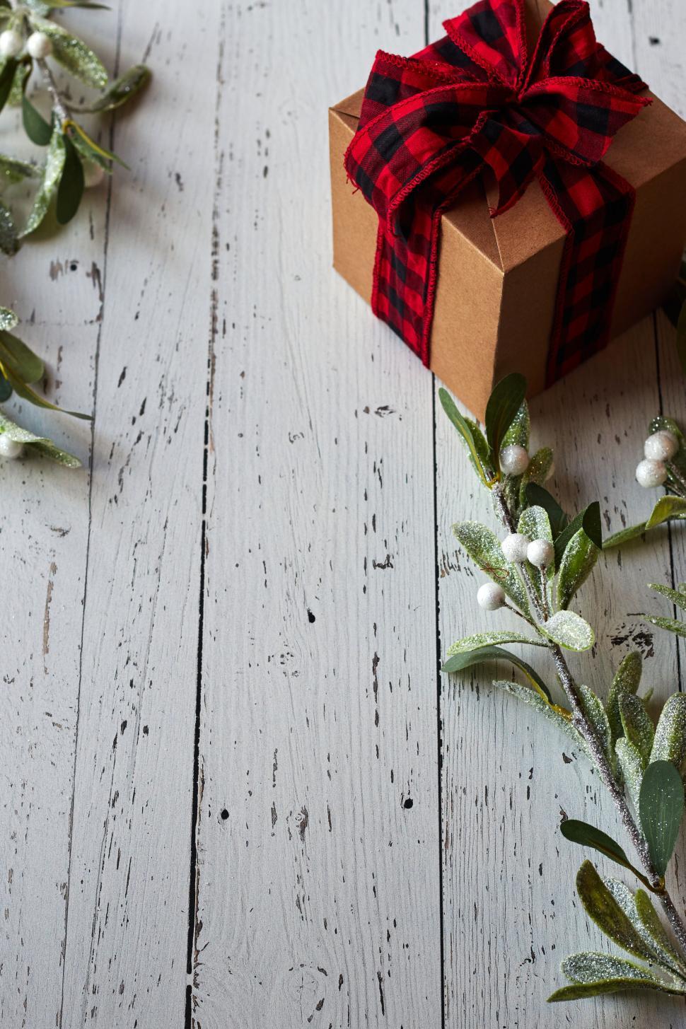 Free Image of Gift wrapped with red plaid ribbon on weathered, white wood. 