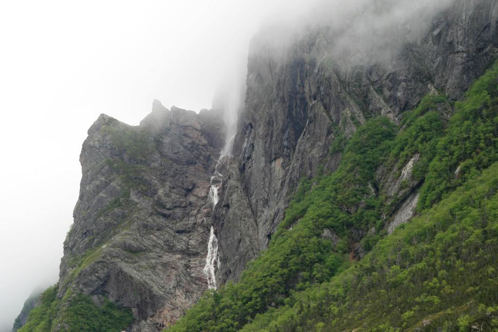 Free Image of Misty mountain landscape with a waterfall and greenery. 