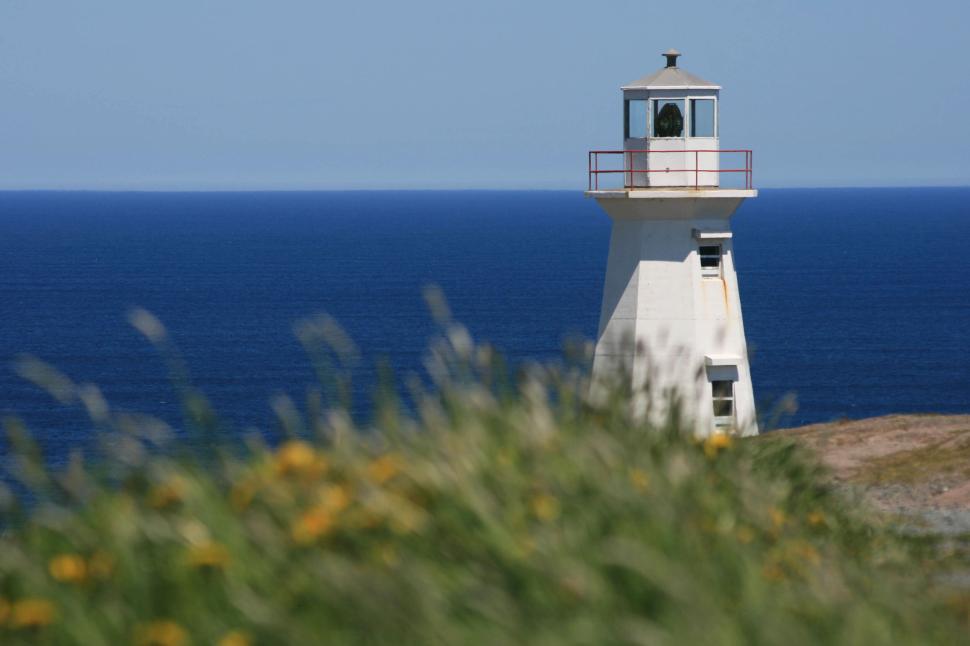 Free Image of White lighthouse beside ocean with clear blue sky 