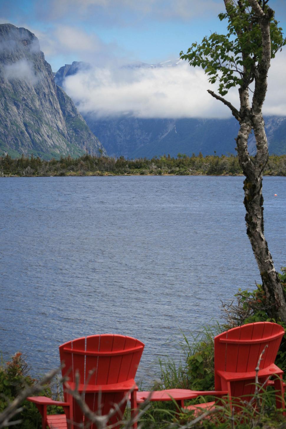 Free Image of Two red chairs facing a lake and mountain view. 
