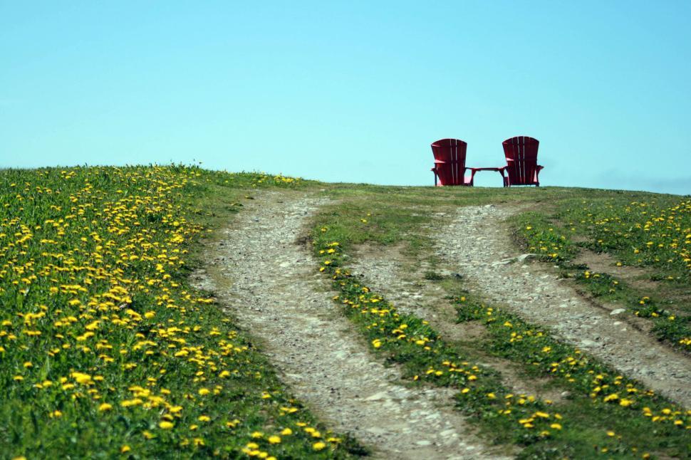 Free Image of Two red chairs on grassy hill beside dirt road path. 