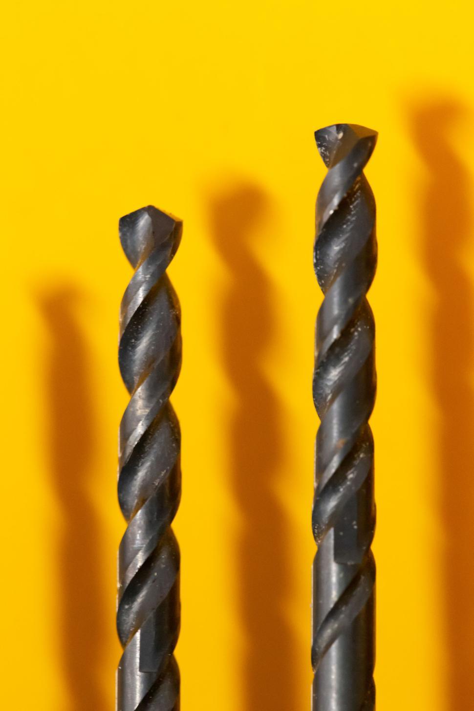 Free Image of Two metallic drill bits with yellow background 