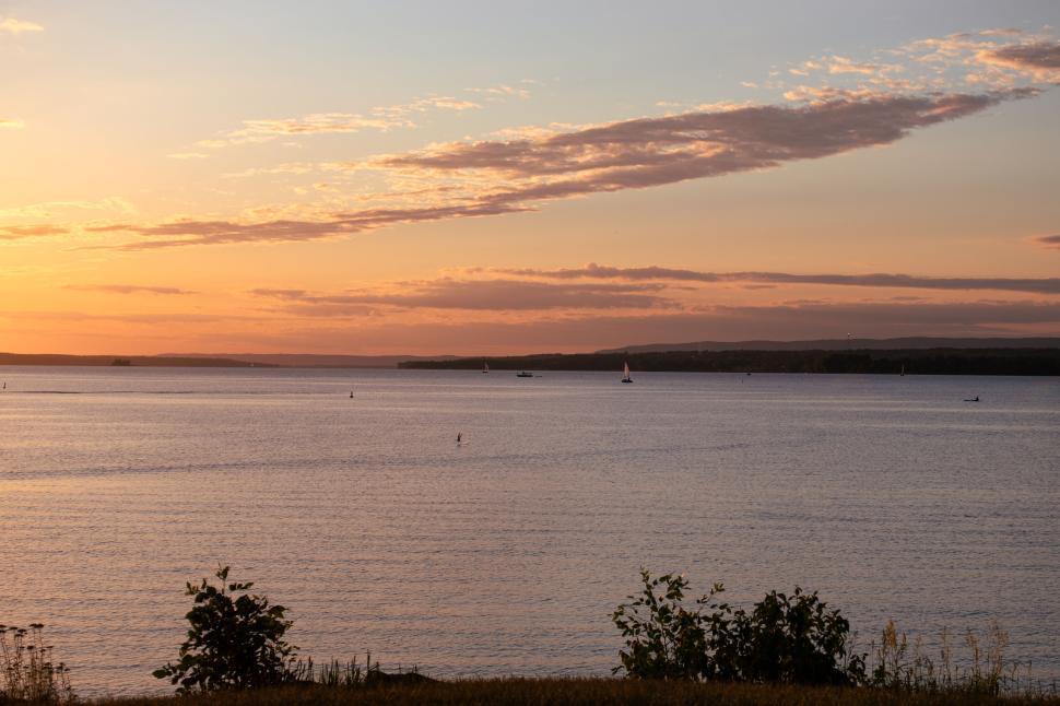 Free Image of Beautiful sunset over calm water with sailboats faraway. 
