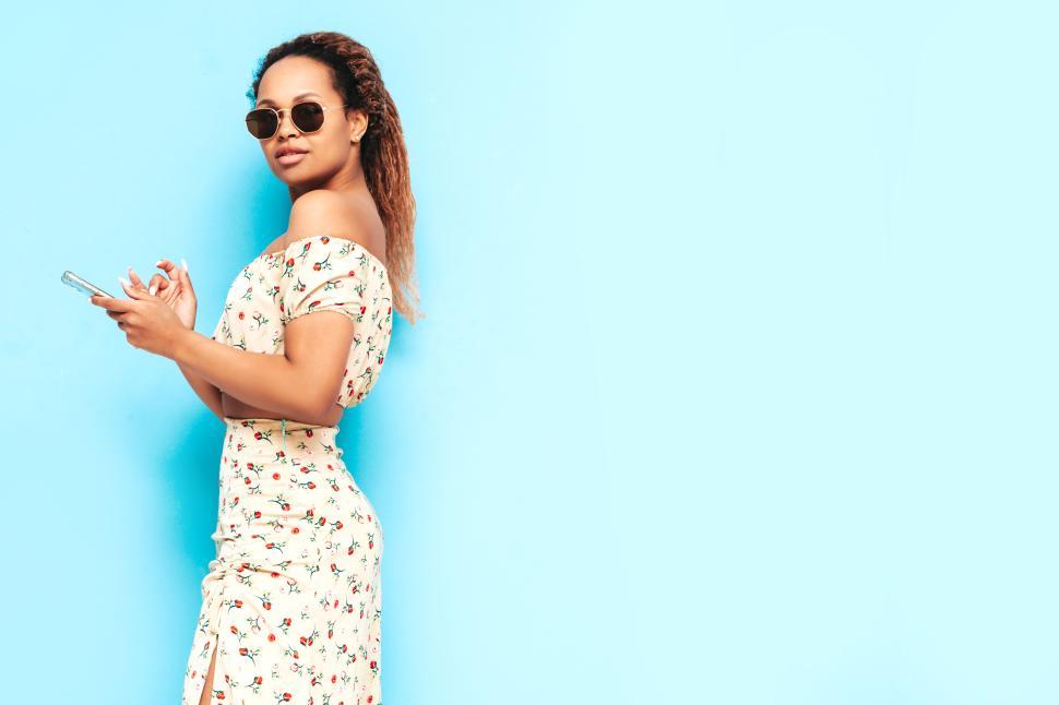 Free Image of Woman in floral outfit with sunglasses and phone. 