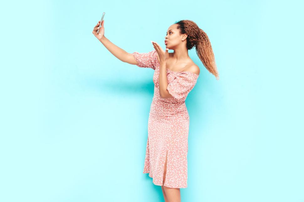 Free Image of Woman taking selfie against blue wall, playful pose. 