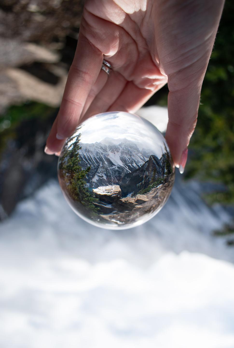 Free Image of Crystal ball handheld revealing upside down mountain view 