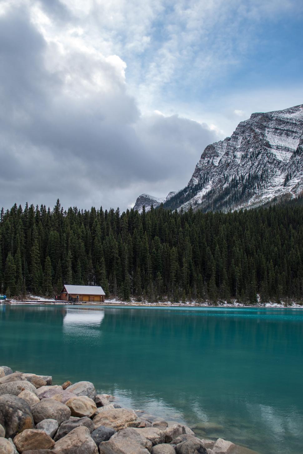Free Image of Cabin by the lake surrounded by mountains and trees. 