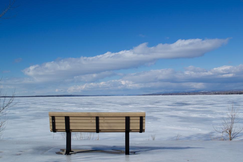 Free Image of Lonely bench facing a vast frozen lake under blue sky. 