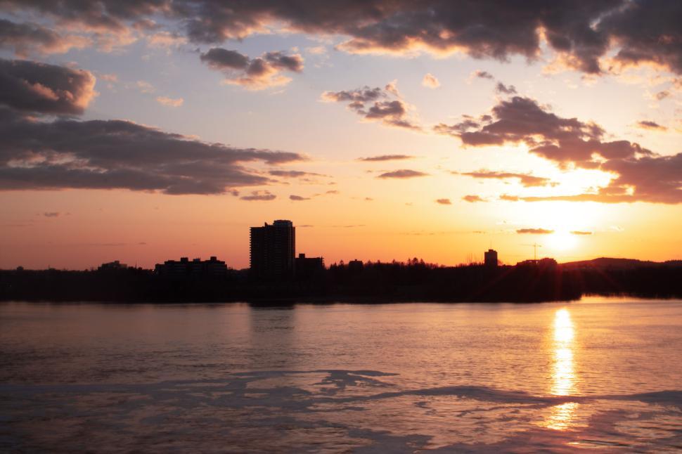 Free Image of Dramatic sunset over calm water with city skyline. 