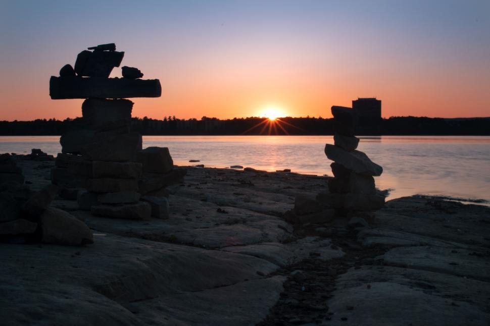 Free Image of Stone cairns along shoreline at sunset with calm waters 