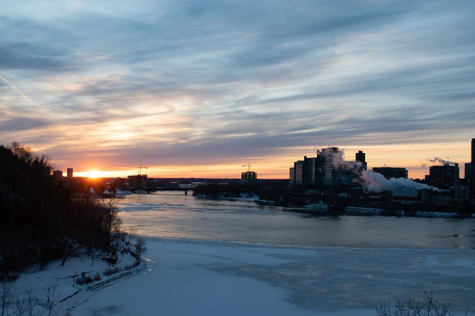 Free Image of Sunset Over a Iced River With Cityscape Background View. 