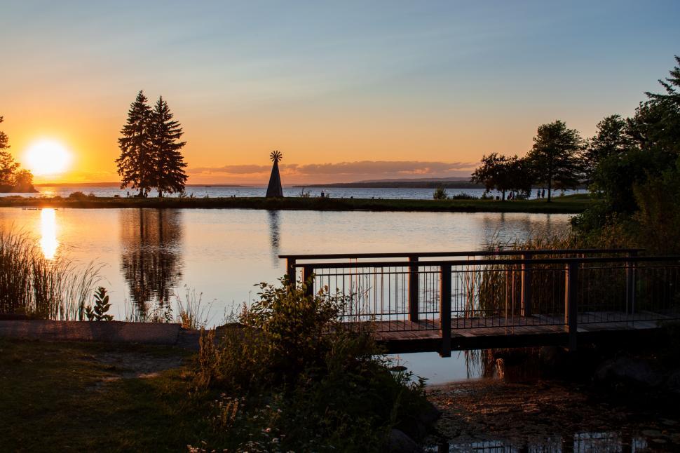 Free Image of Sunset over calm lake with bridge in foreground view 