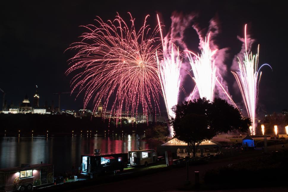 Free Image of Nighttime fireworks display over calm reflective river. 