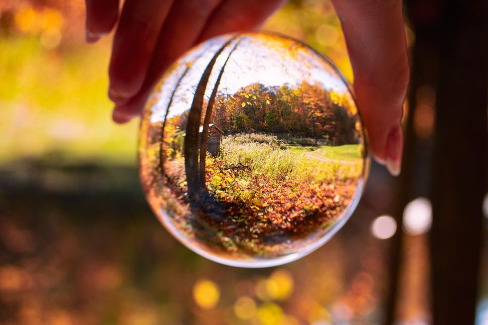 Free Image of Hand holding glass sphere reflecting autumn landscape. 