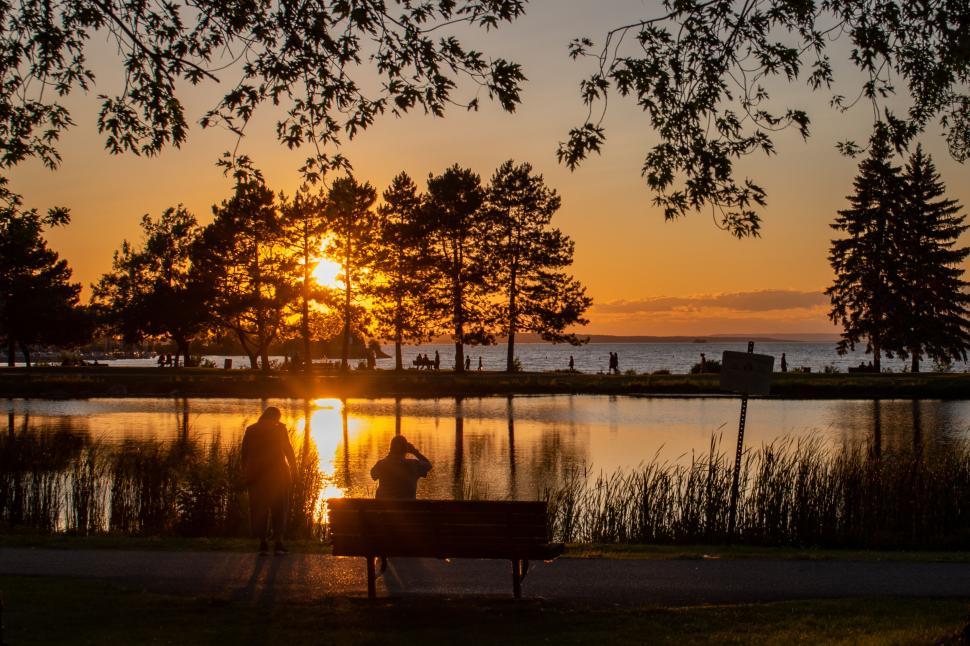 Free Image of Sunset by a lakeside park with people silhouette 