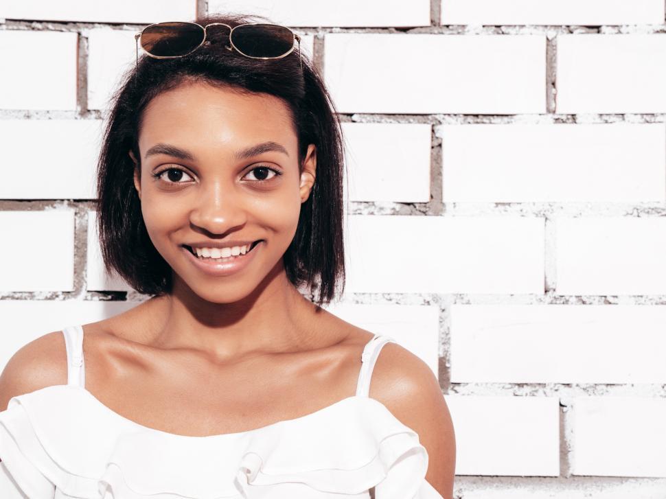 Free Image of Close-up of woman smiling by white brick wall outside. 
