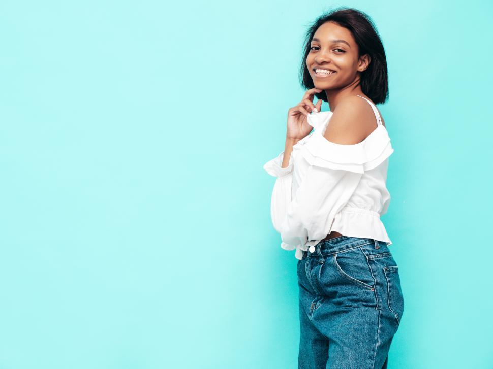 Free Image of Happy woman in white top posing against blue backdrop. 