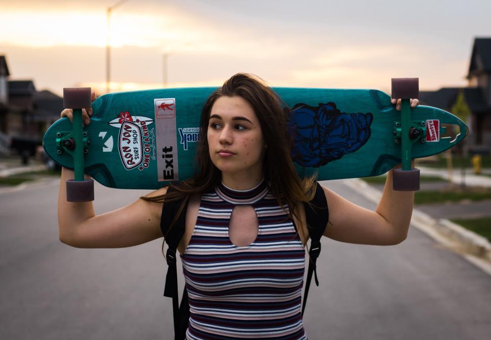 Free Image of Young woman holds skateboard over shoulders outdoors. 