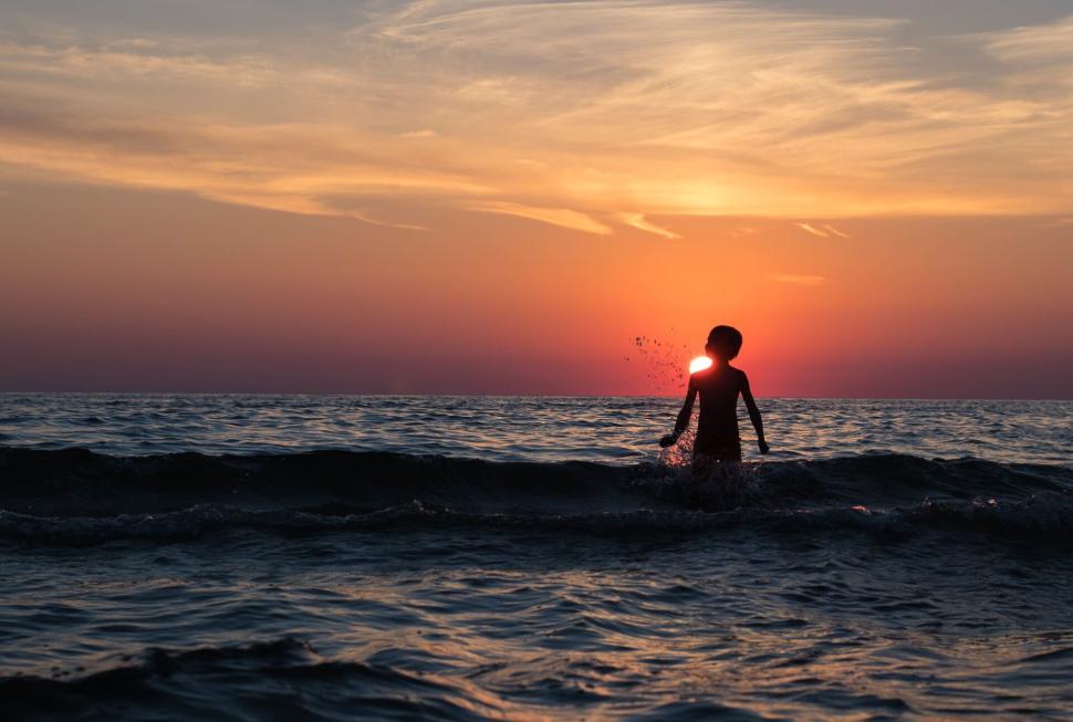Free Image of Silhouette of person in ocean water during sunset. 