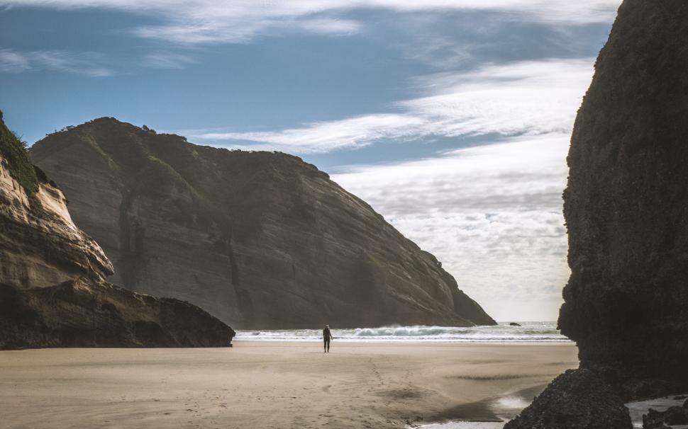 Free Image of Person walking on isolated beach with high cliffs view 