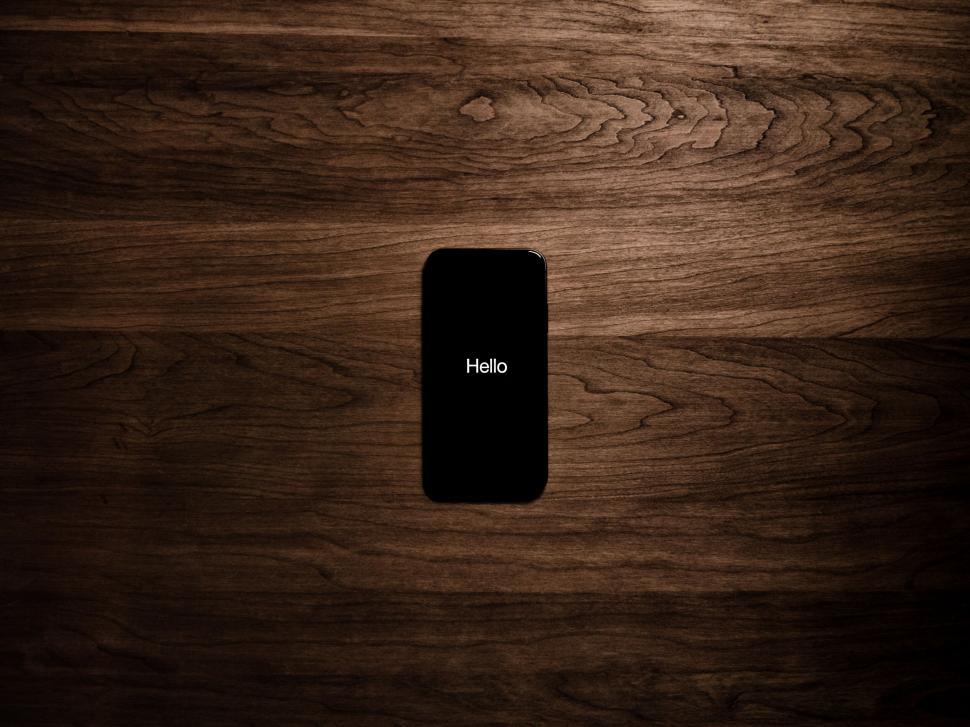 Free Image of Smartphone on wooden surface with illuminated  Hello  screen 