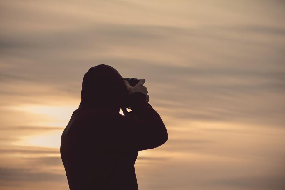 Free Image of Silhouette of person photographing sunset behind cloudy sky 