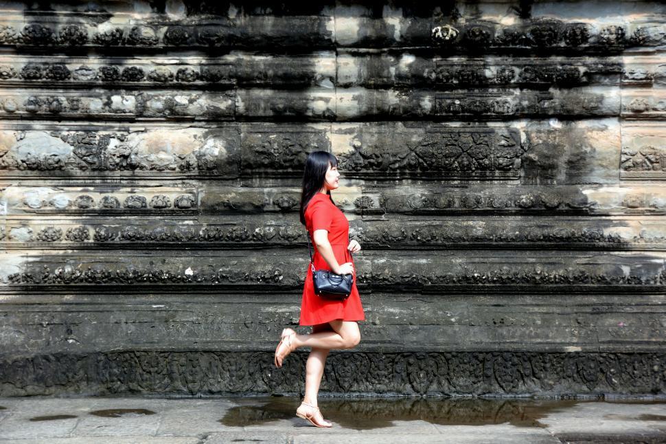 Free Image of A lady in a red dress posing against ancient stone wall 