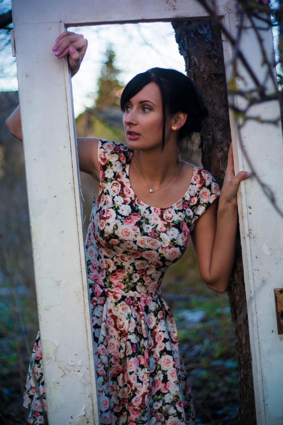 Free Image of Woman in floral dress looking through door frame outside 