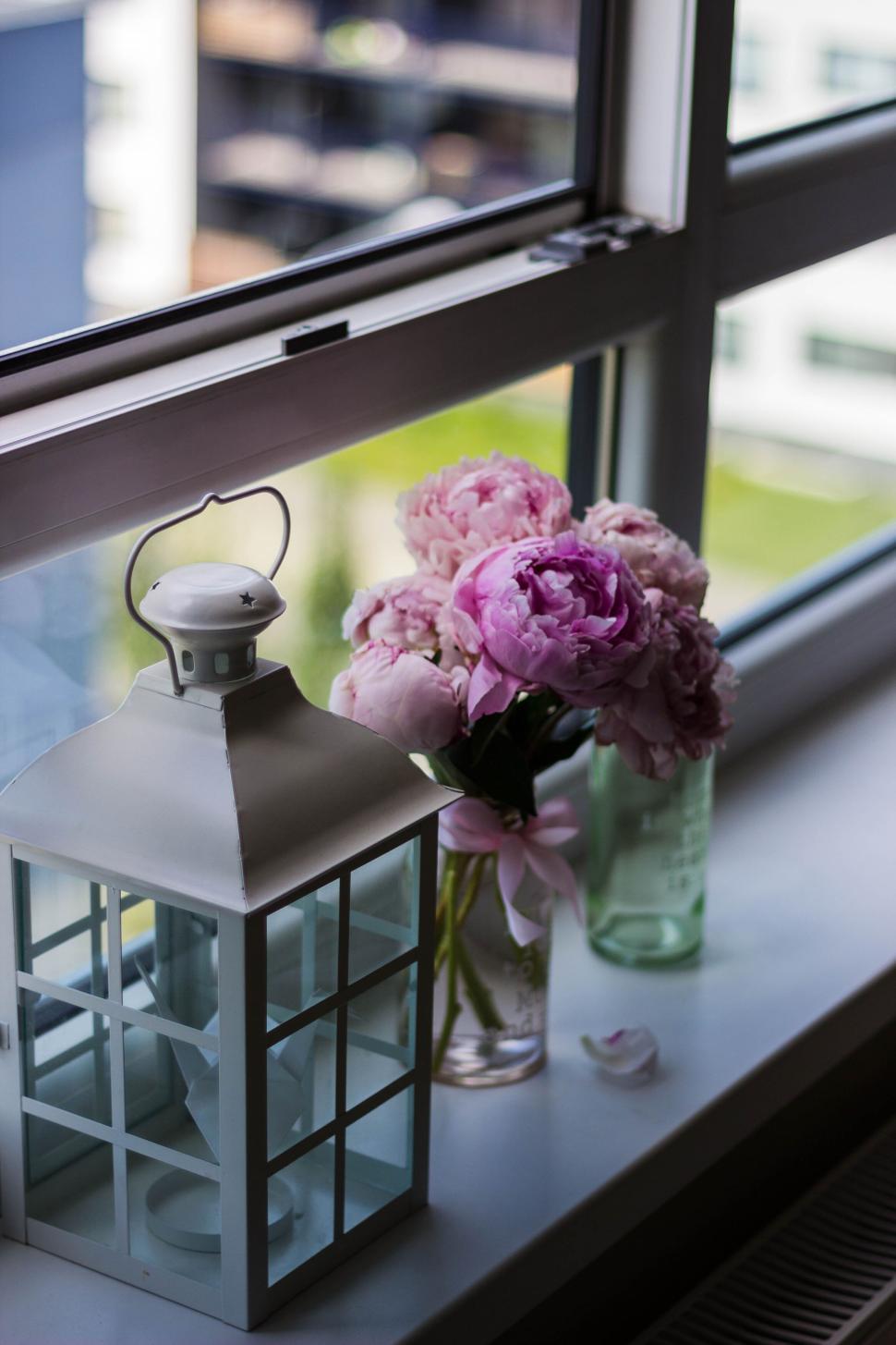 Free Image of Pink peonies in a glass jar by a white lantern on window 