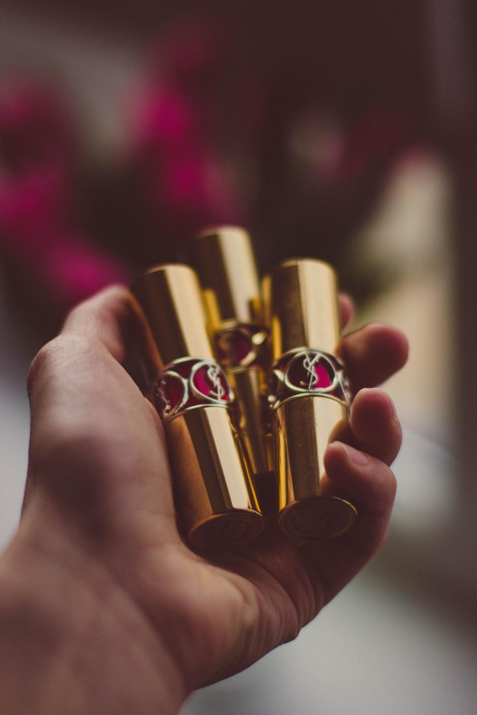 Free Image of Hand holding three golden lipstick tubes elegantly 