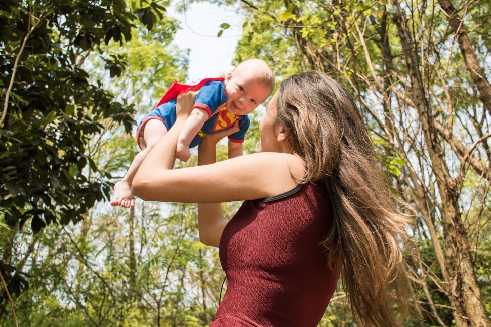 Free Image of Woman lifting baby in hero costume outdoors, bond. 