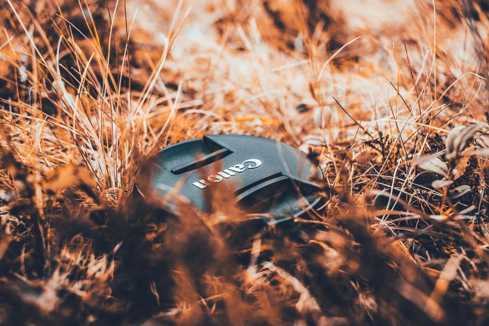 Free Image of Canon camera lens cap amidst an autumnal dry grass field 