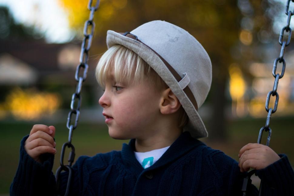 Free Image of Blond child on a swing wearing a stylish cream hat. 