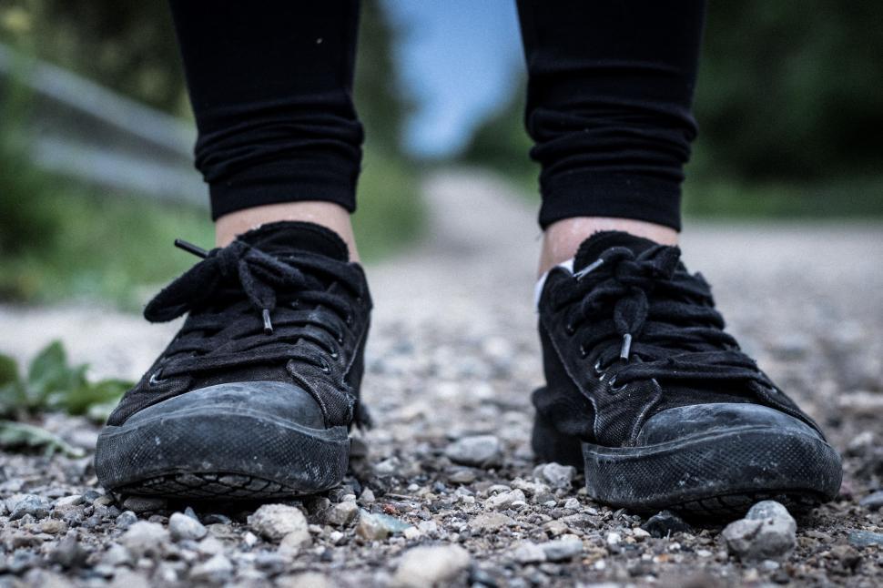 Free Image of Close-up of worn black sneakers on a rocky dirt path 