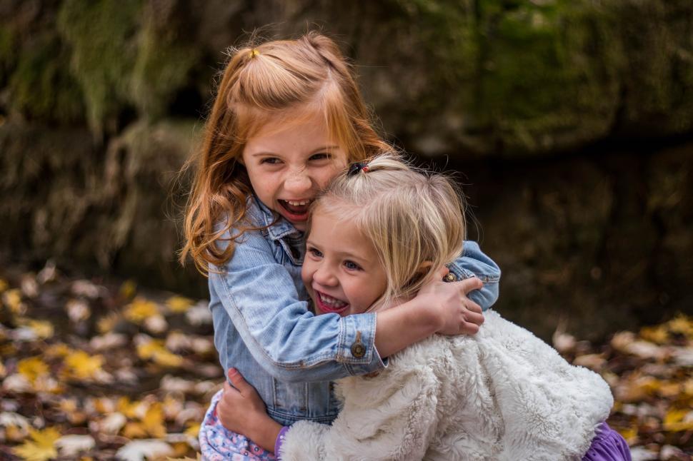 Free Image of Two young girls hugging and laughing in autumn leaves. 