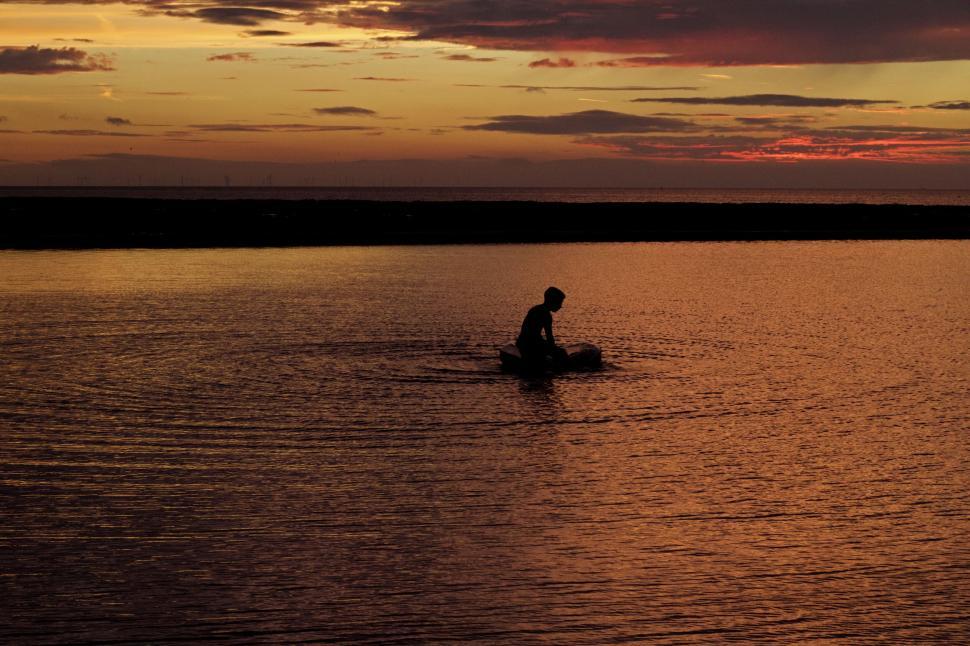 Free Image of Silhouette of person wading in water during sunset. 