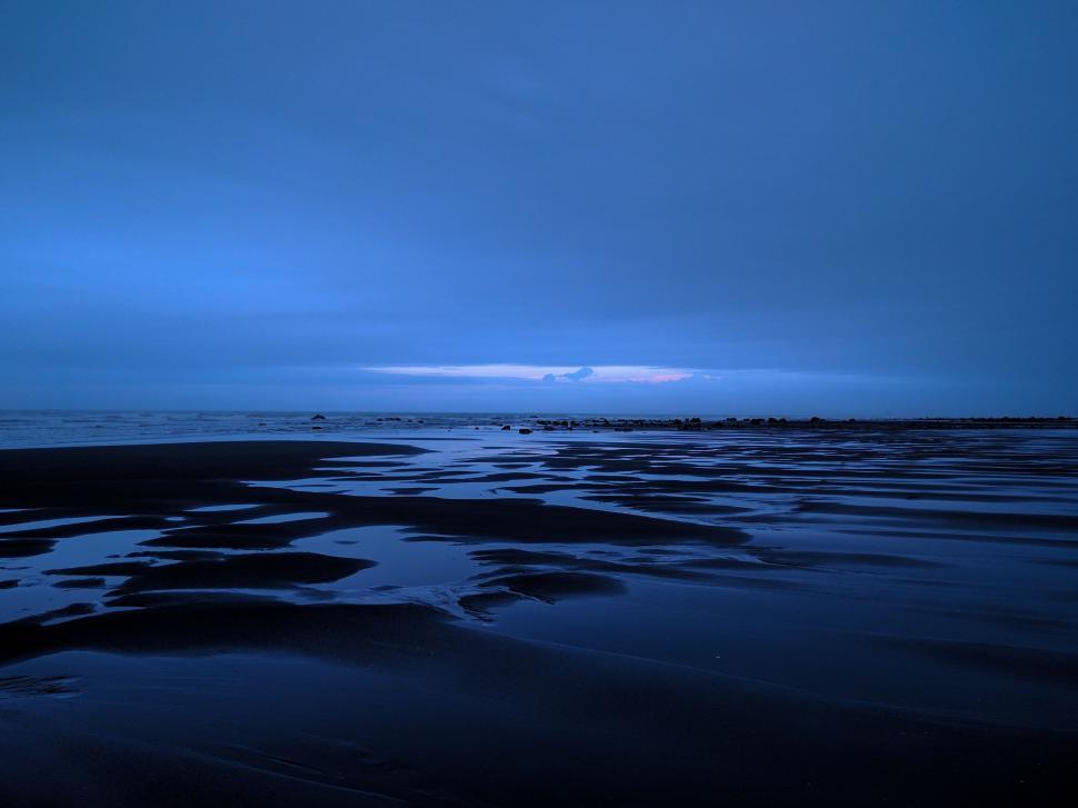 Free Image of Dusk settles over serene beach with calm reflective sands 
