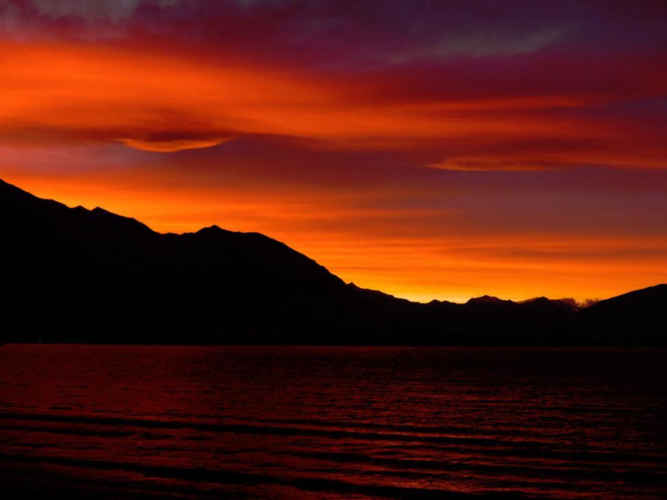 Free Image of Vibrant sunset over calm sea with black silhouettes 