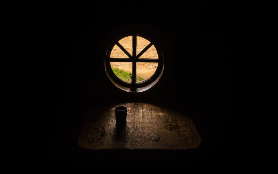 Free Image of Circular window casting light in dark room with table 