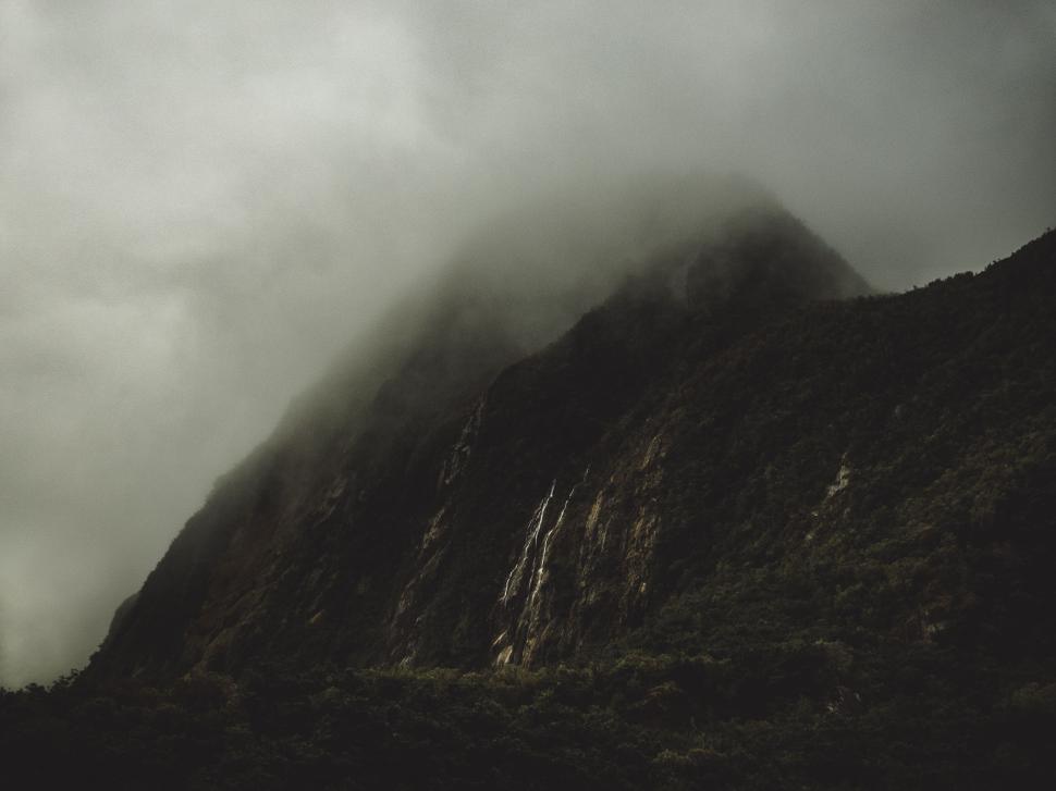 Free Image of Misty mountain with dense forest and cascading waterfall 