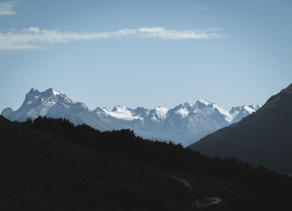Free Image of Snow-capped mountains with shadowed foreground trees 