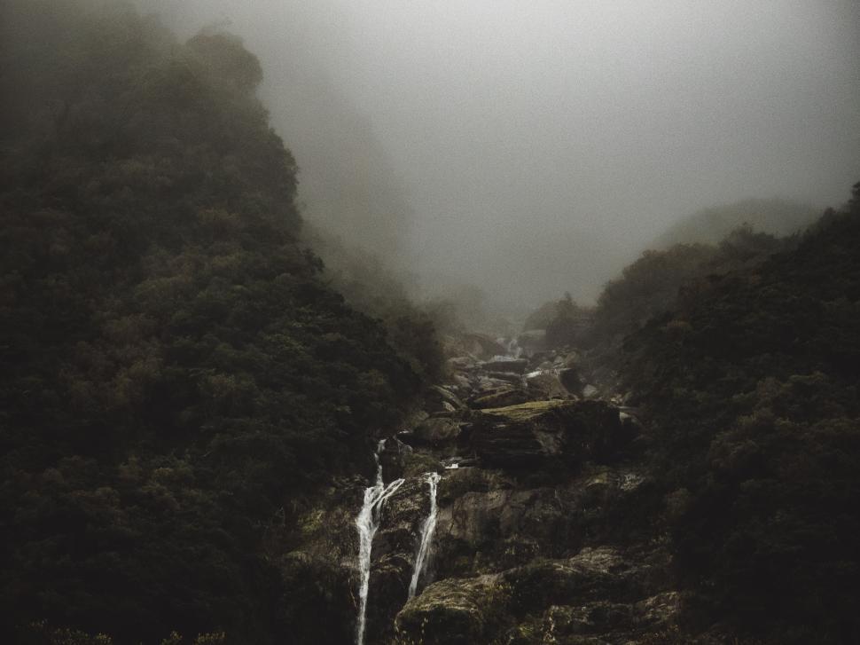 Free Image of Foggy forested mountain with cascading waterfall 