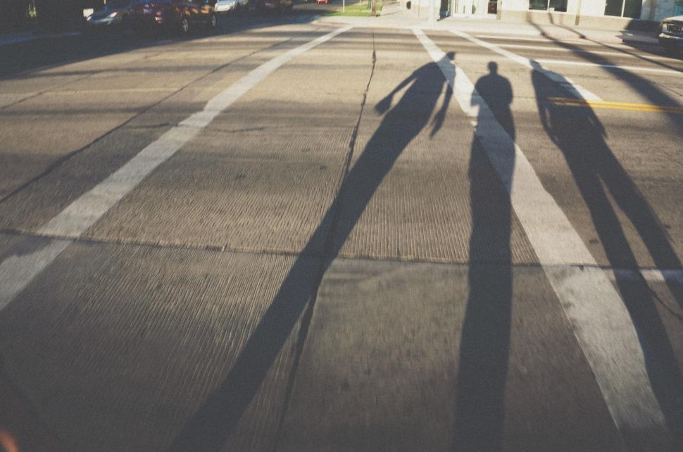 Free Image of Shadows of three people cast on urban street at sunset 