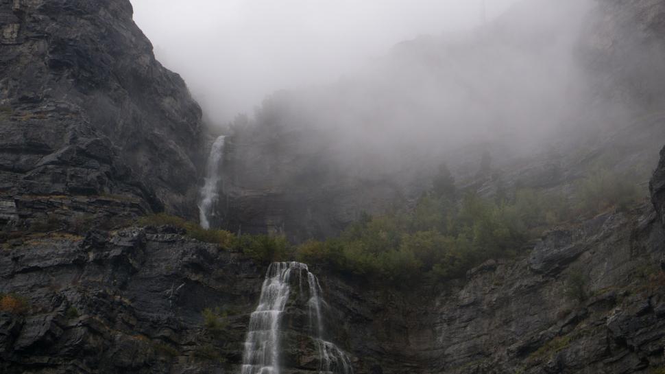 Free Image of Waterfalls cascading down rocky mountain in fog 