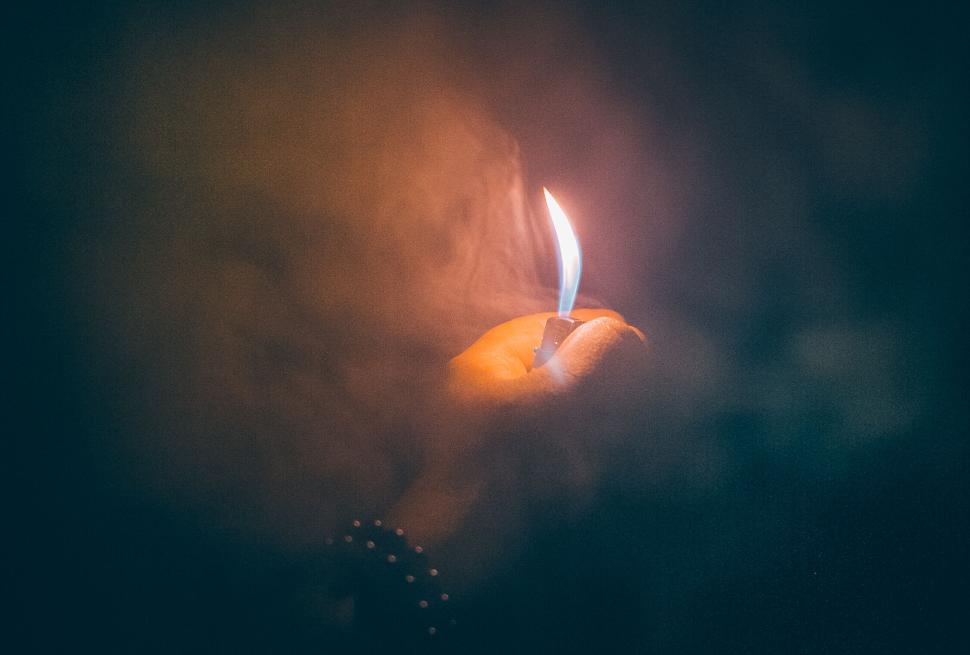 Free Image of A hand holding a lighter with flame amidst smoke. 