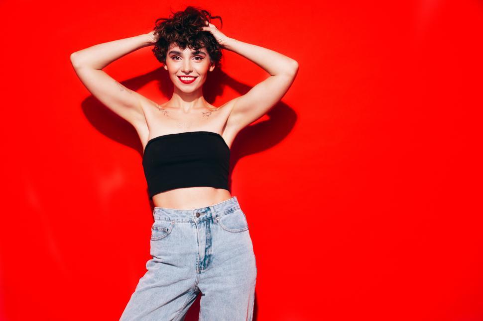 Free Image of Cheerful woman posing with hands in hair, red backdrop. 