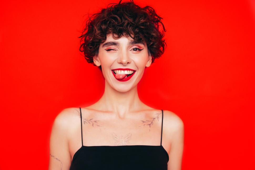 Free Image of Winking woman with tongue out, playful red backdrop. 