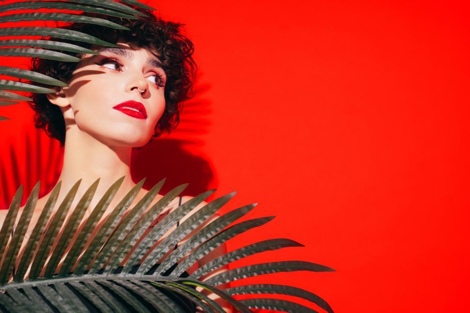 Free Image of Contemplative woman with palms against bright red background 